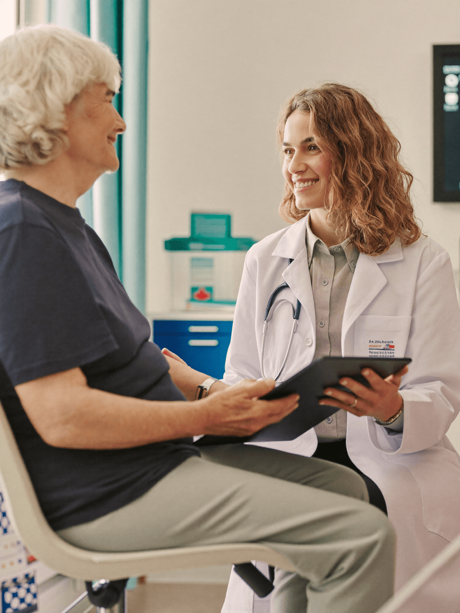 A physician sitting with an older patient in a bright clinic room, reviewing care information together